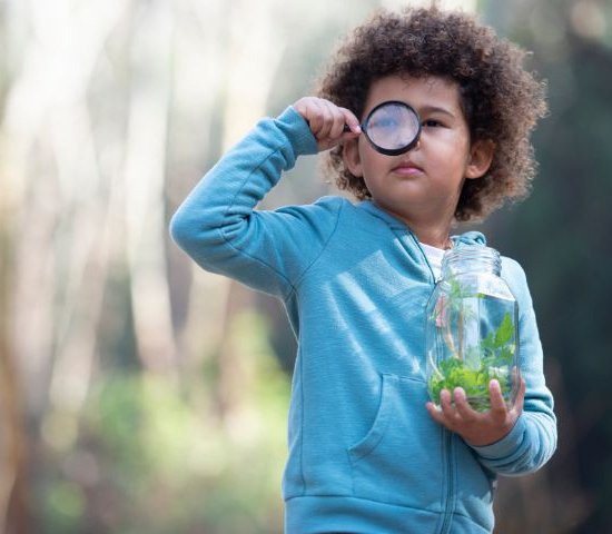 a child holds a jar of water looking through a magnifying glass