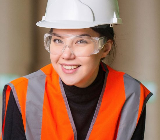 a young woman wearing a reflector vest and hard hat, employee of a manufacturing company