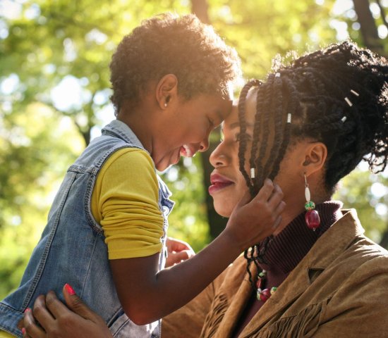 a young mother and her daughter smile and hug in a forested area