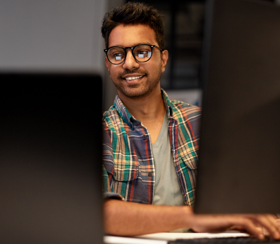 Young man with glasses smiling and looking at a computer