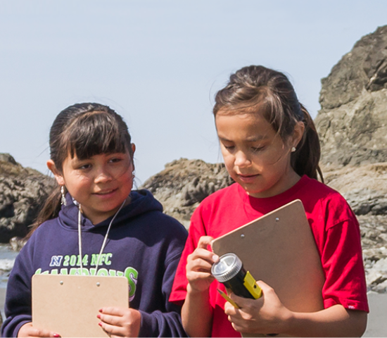 Two young girls outdoors looking at water samples and taking notes