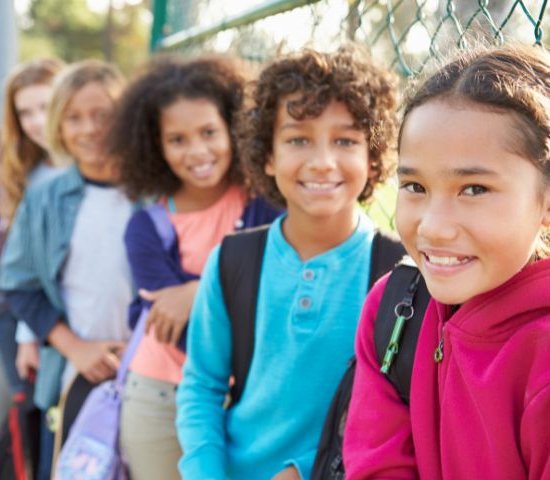 a diverse group of young students stands in a line along a fence all smiling