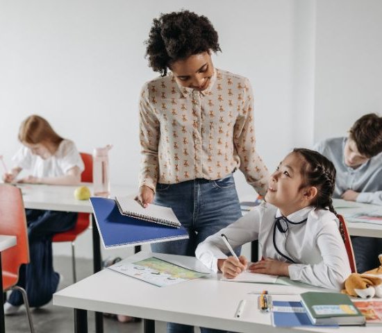 a female teacher speaks with a girl student at her desk