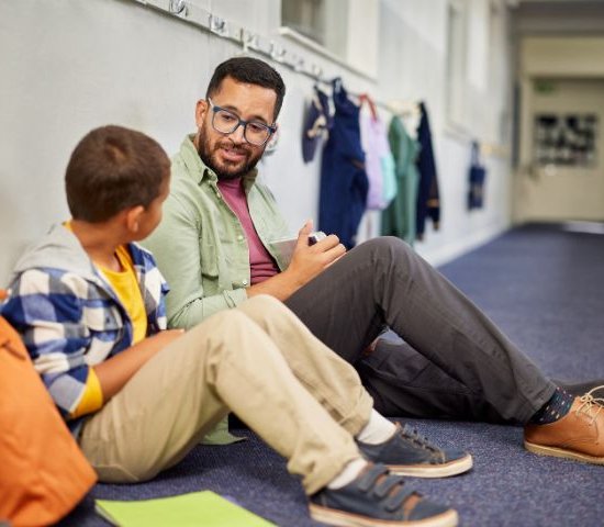 a teacher sits with a student for a discussion in a hallway