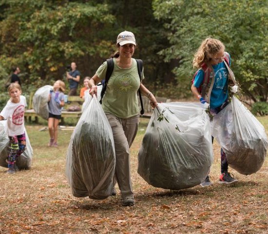 a woman and young girls carry bags full of debris at a volunteering event