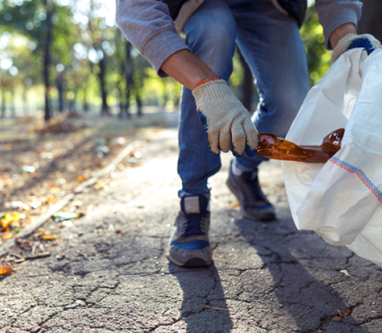 Person putting plastic bottle in garbage bag for national public lands day volunteer clean up event.
