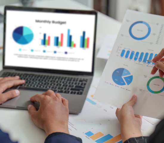 Two people's hands holding financial reports and typing on a laptop