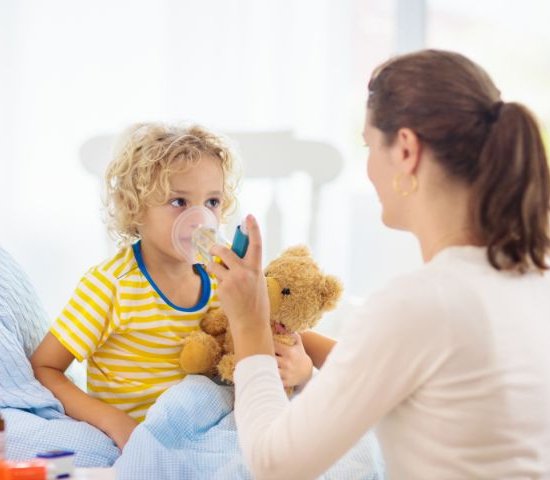 a young boy uses an asthma inhaler administered by a parent