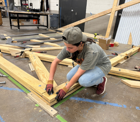 Person crouching on a cement floor working with wood planks