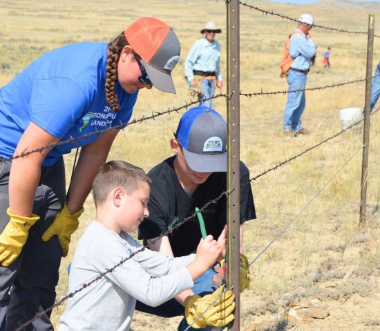 a volunteer leader instructors two young volunteers on fence repair