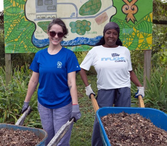 two women volunteers stand side by side holding wheelbarrows full of mulch