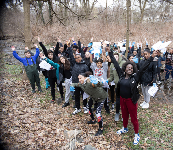 Middle school students outdoors with arms in the air and happy