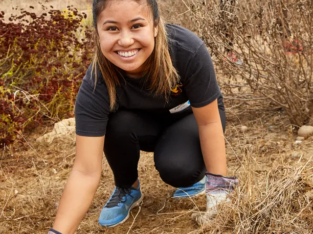 Young woman with gloves smiling and removing weeds