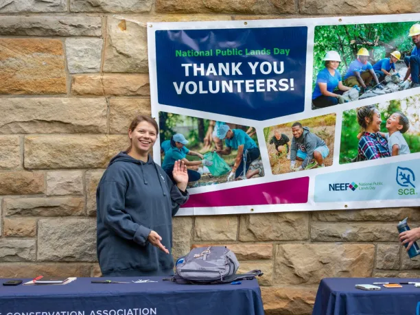 Two national public lands day volunteers stand near a NPLD banner that say Thank You Volunteers