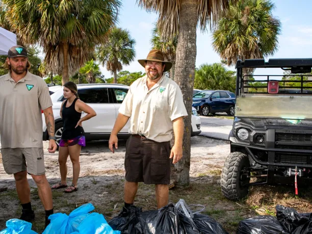 Bureau of Land Management site manager stands with collected trash in bags during national public lands day event