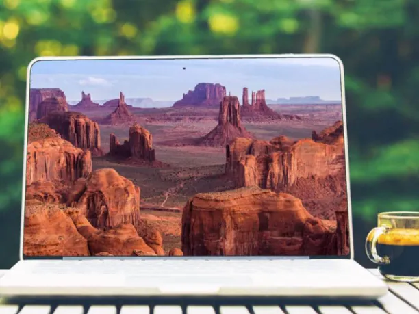 Laptop with canyonlands on screen sitting outdoors on table with coffee cup next to it