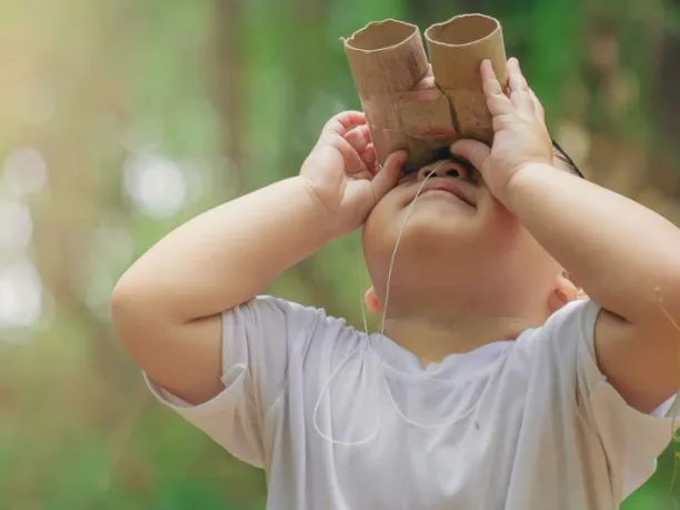 Young child outdoors with paper bionoculars looking up 
