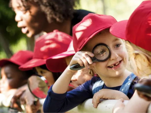 Child looking through a magnifying glass at others.