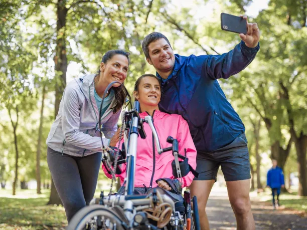 a woman sitting on a wheelchair bike take a selfie with a man and woman standing next to her.