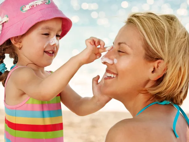 a young girls with sunscreen on her face puts sunscreen on her mother's face
