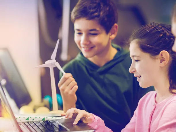 three students work on a laptop while holding a small wind turbine