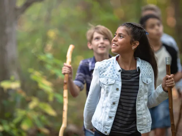 a group of young students walks through a forest using walking sticks