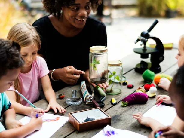 an environmental educator holds a seedling in a jar as part of an environmental education lesson with some students