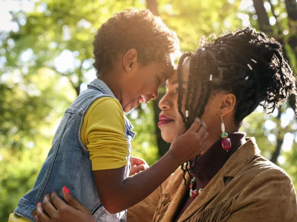 a young mother and her daughter smile and hug in a forested area