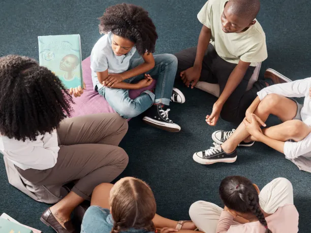 Teacher holding book sitting in a circle with students on the floor