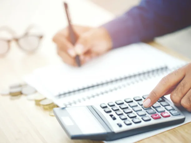 Person with pen and paper using a calculator