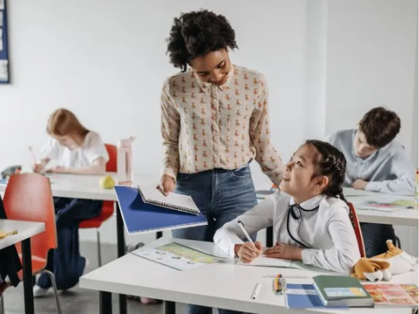 a female teacher speaks with a girl student at her desk