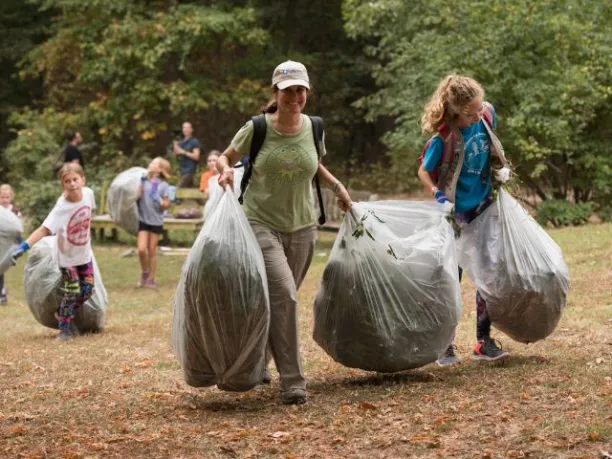 a woman and young girls carry bags full of debris at a volunteering event