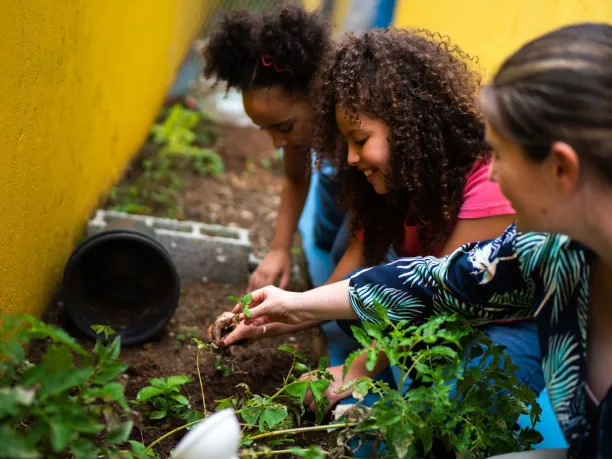 a female teachers plants a school garden with two young students