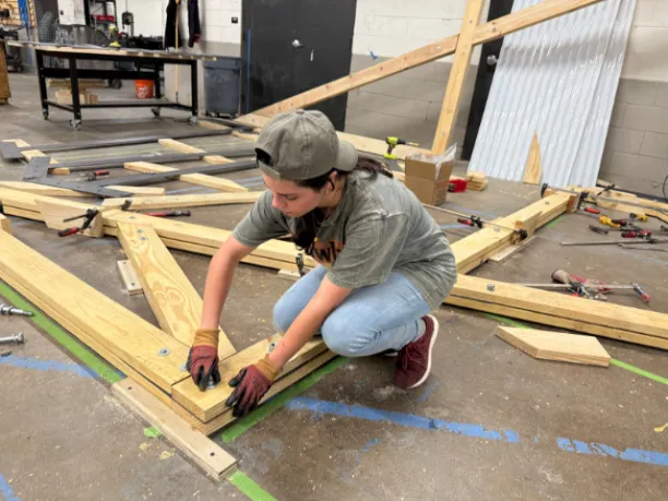 Person crouching on a cement floor working with wood planks