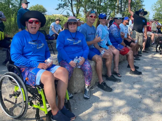 a man using a wheelchair sits with family and friends waiting for a kayak launch