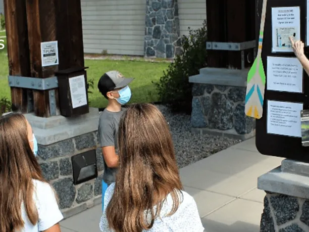 Forest Service staff pointing to announcement board instructing group of middle school students. 