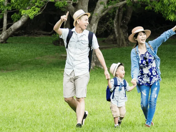 Family with young son walking and pointing to things on a trail in a green field near