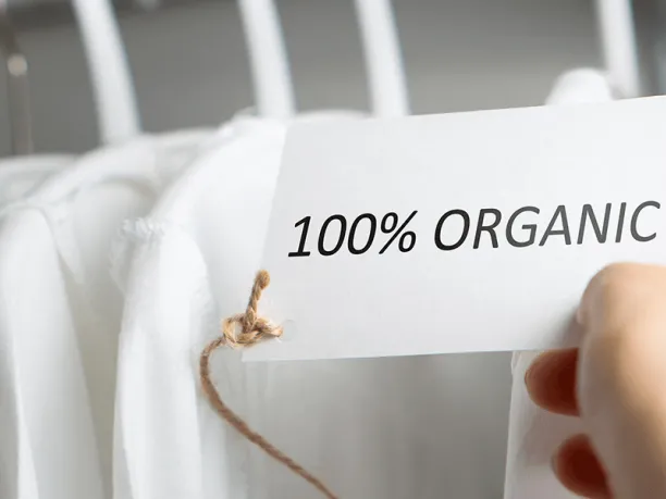 rack of white shirts and hand holding an ecolabel that reads 100% organic