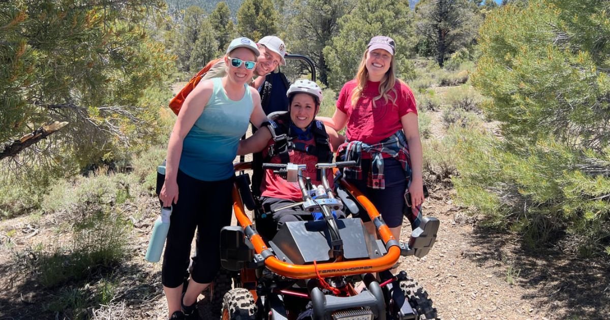 a woman sits in an all terrain wheelchair surrounded by a group of people on the trail 