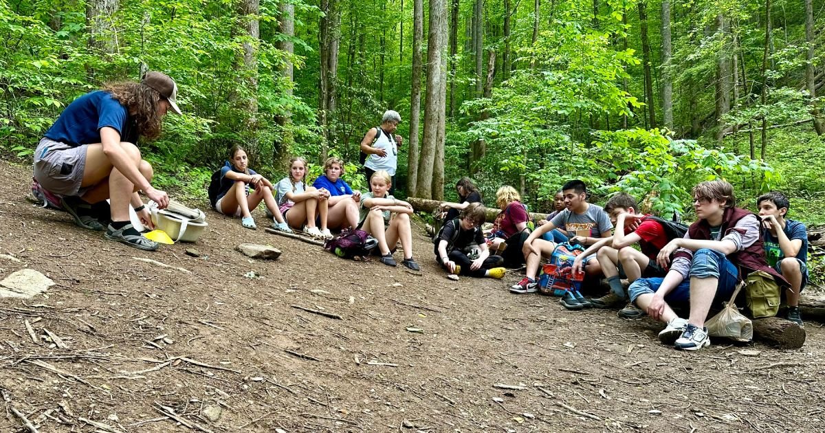 a group of students sits on the forest floor for a Greening STEM outdoor education lesson