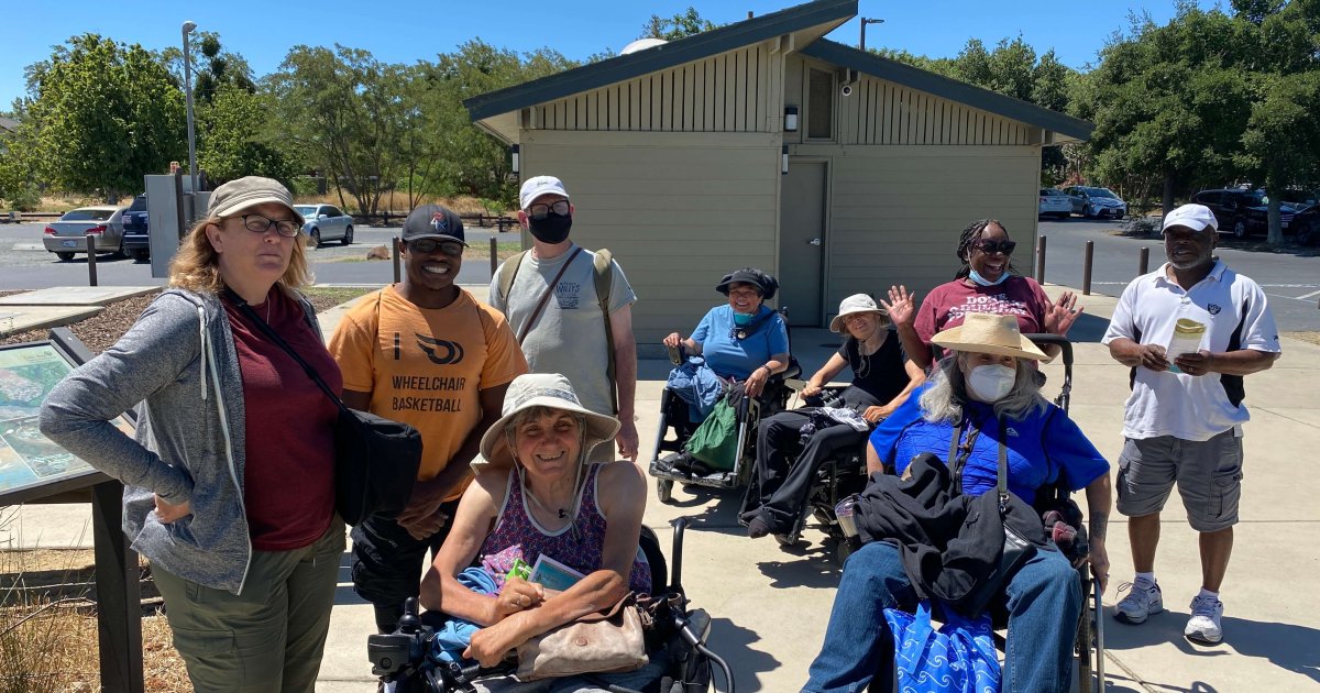 A racially diverse group of people with various physical disabilities including some in wheelchairs, arrive at Big Break Regional Shoreline for All Abilities Day 