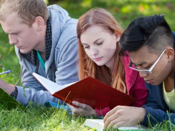 Three teens lying on the grass reading