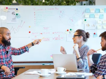 Photo of diverse group of professionals talking around a whiteboard.