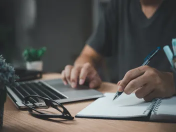 Person typing on computer while writing on a notepad