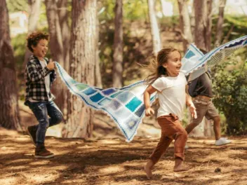 Two children holding a blanket up and running through the forest