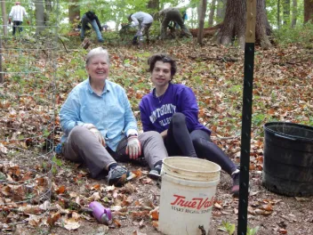 Two people sitting on the ground with a clean up bucket nearby