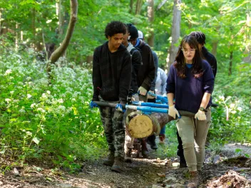 A diverse group of young people carry a large log to place on trail during National Public Lands Day event.