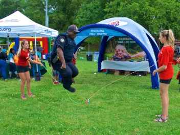 Police officer jumping rope being held by two volunteers