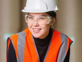 a young woman wearing a reflector vest and hard hat, employee of a manufacturing company