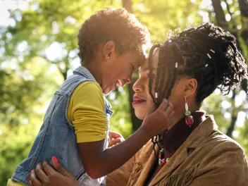 a young mother and her daughter smile and hug in a forested area